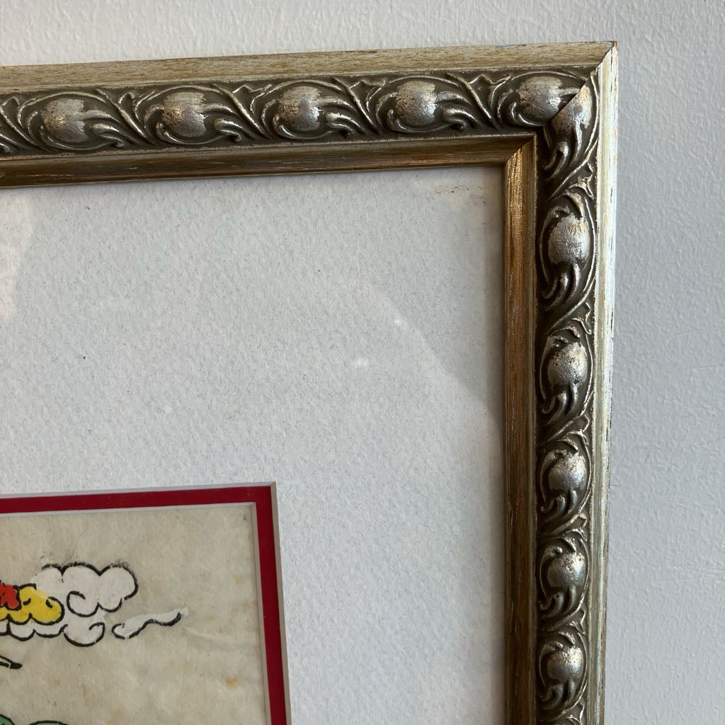 Close-up of a framed artwork with decorative silver frame on a white wall.