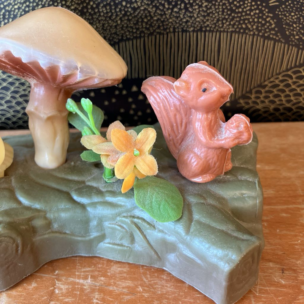 Sculpture of a squirrel, flowers, and a mushroom on a rock-like base.