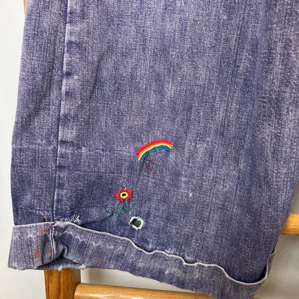 Blue denim jacket with embroidered rainbow and flower design on a white background