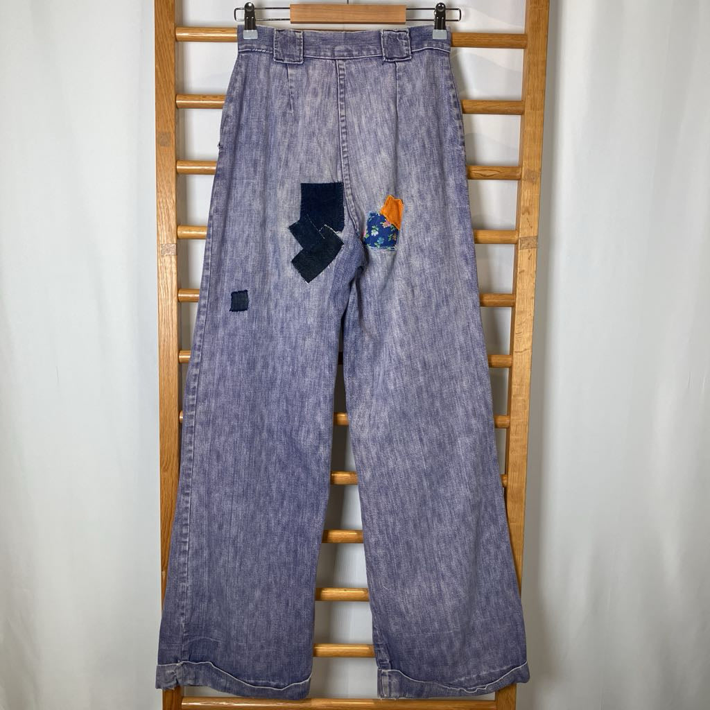 Blue denim jeans with patches on a wooden rack against a white background