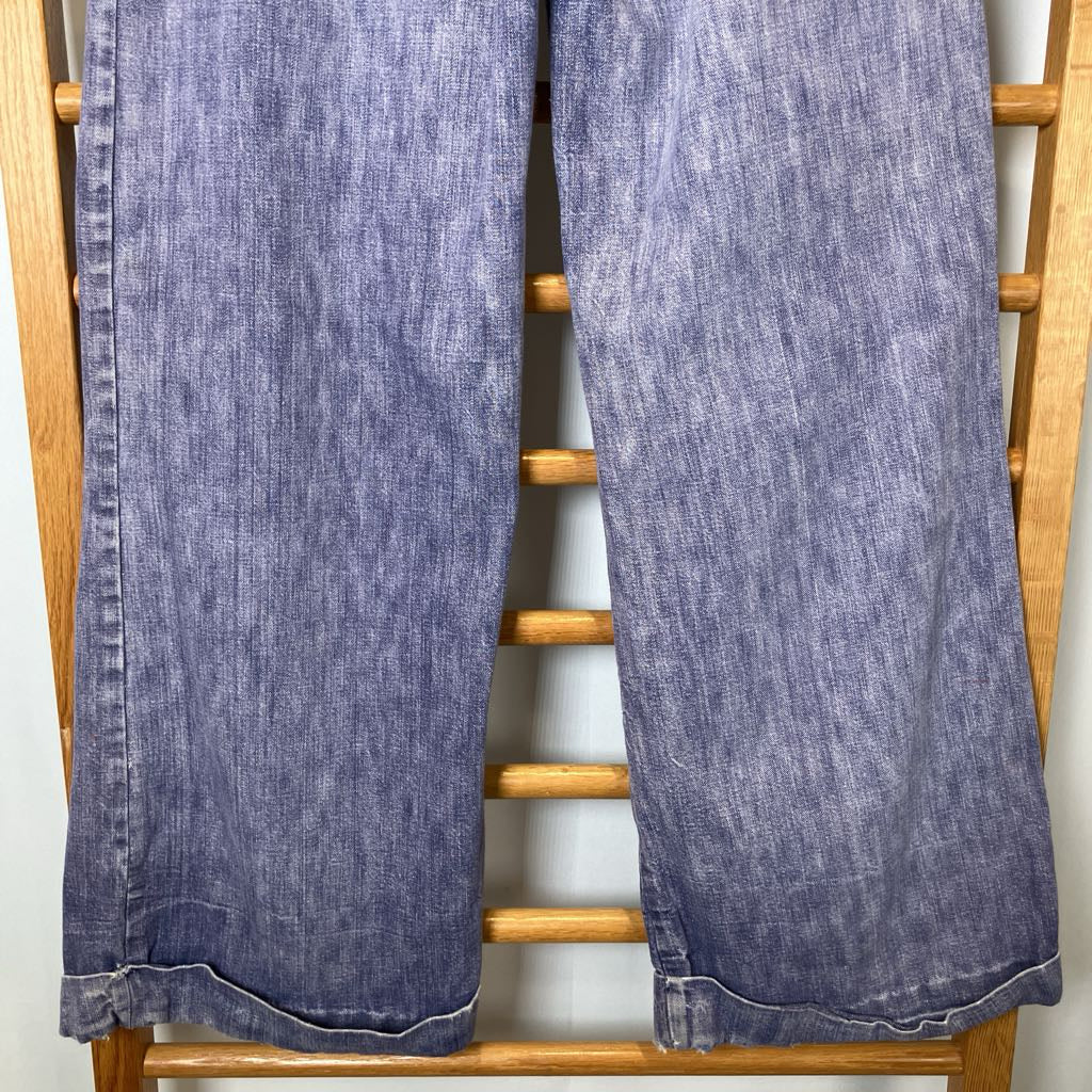 Pair of blue jeans hanging on a wooden rack against a white wall
