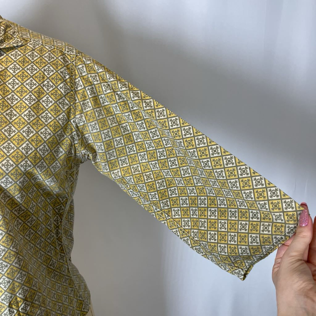 Long-sleeve shirt with a yellow and green geometric pattern held by a hand against a plain background