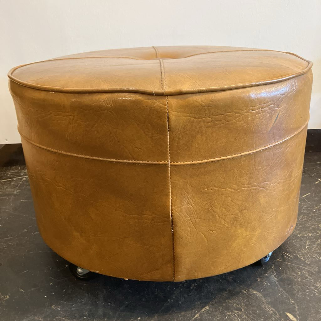 Brown leather ottoman on wheels against a plain background