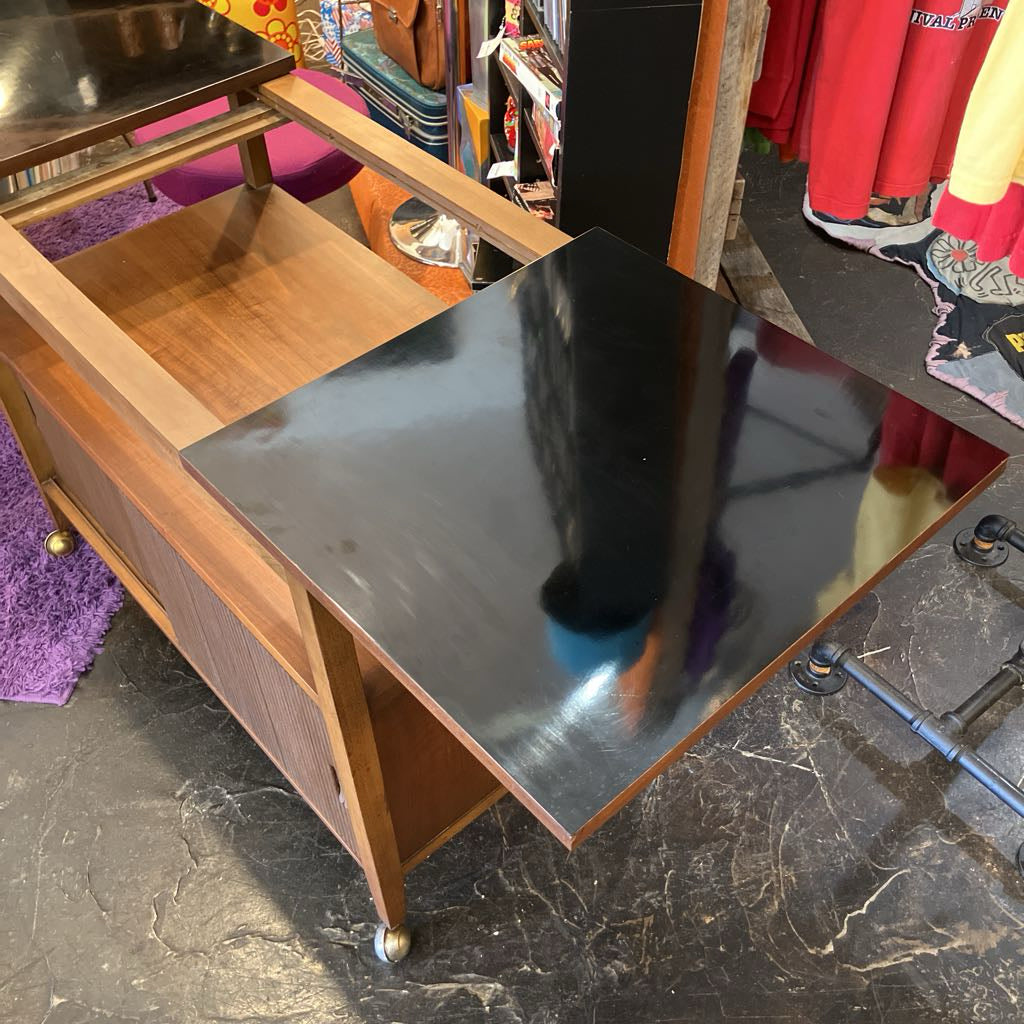 Wooden bar cart with a black countertop in a store setting