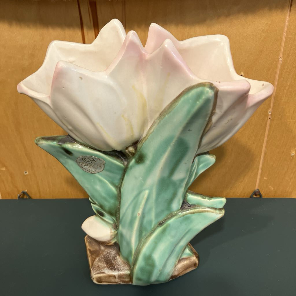 Ceramic tulip flower vase with pink petals and green leaves on a dark surface.