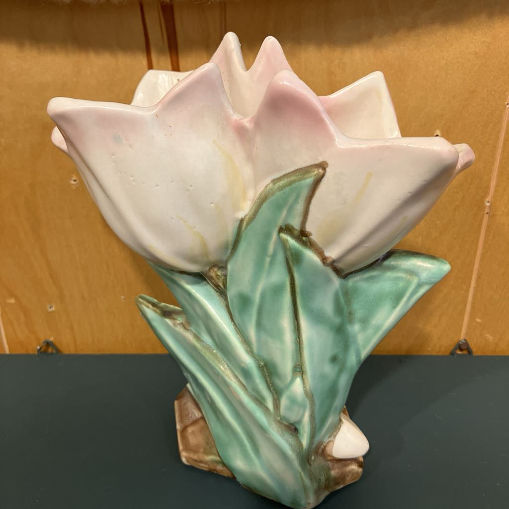 Ceramic tulip vase with pink petals and green leaves on a dark surface.