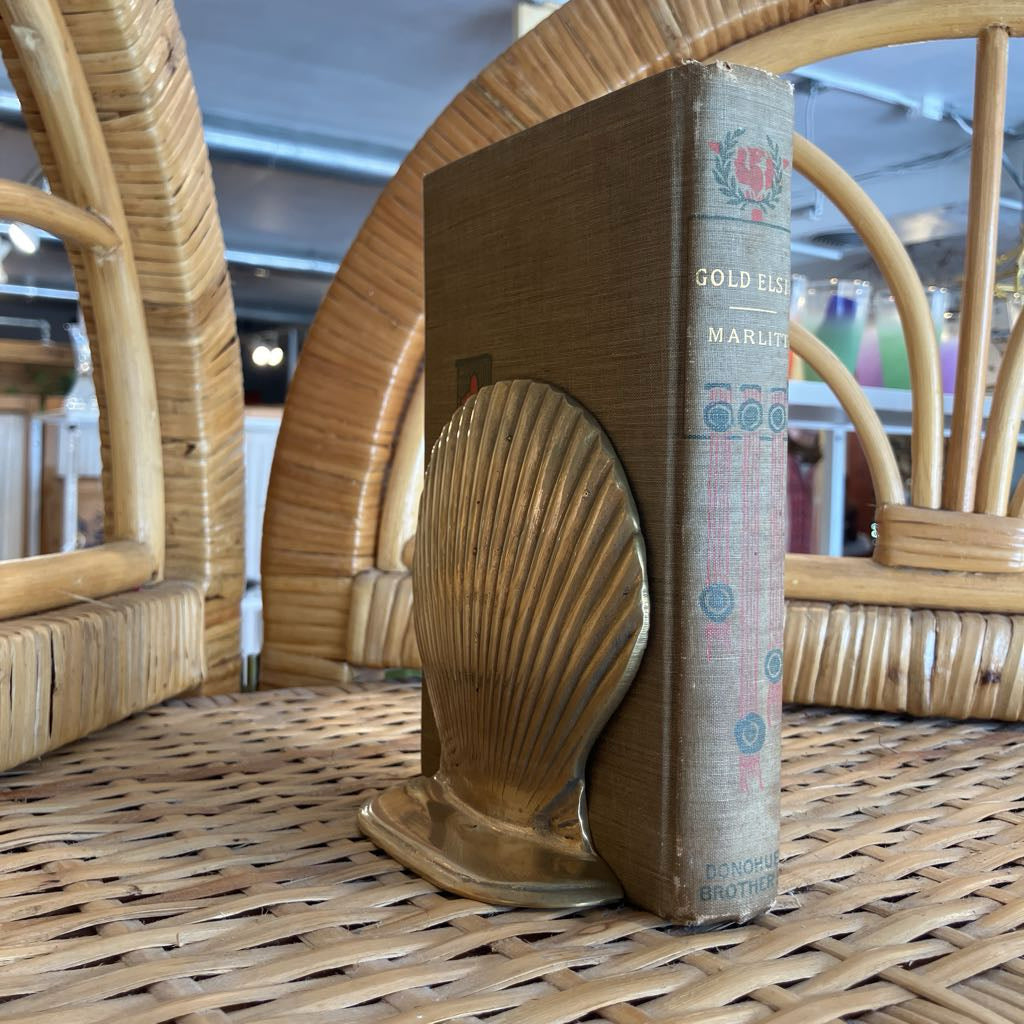 Bookend shaped like a shell holding a book on a wicker surface.
