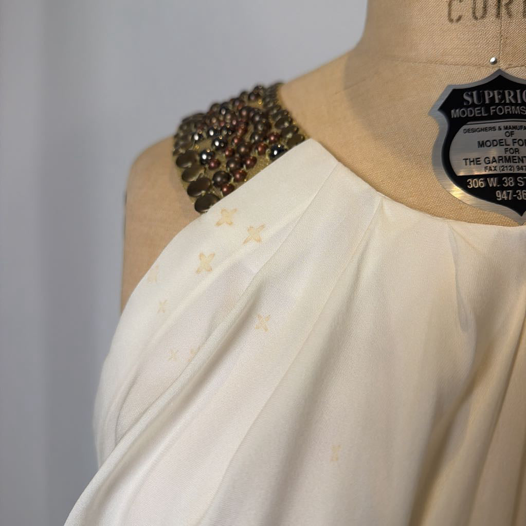 Mannequin wearing a white garment with a decorative shoulder piece on a plain background