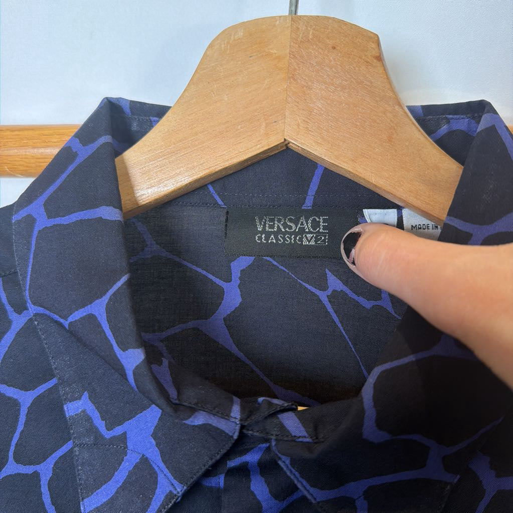 Versace shirt with a geometric pattern on a hanger, held by a hand.