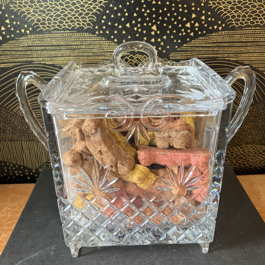 Clear glass candy dish with decorative lid filled with dog treats on a patterned background