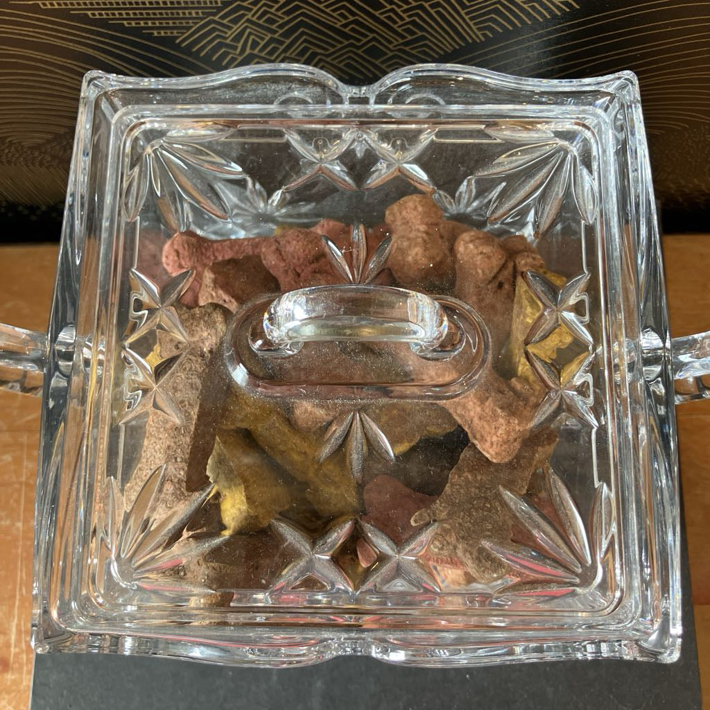 Decorative glass container with star-shaped cutouts filled with small stones.