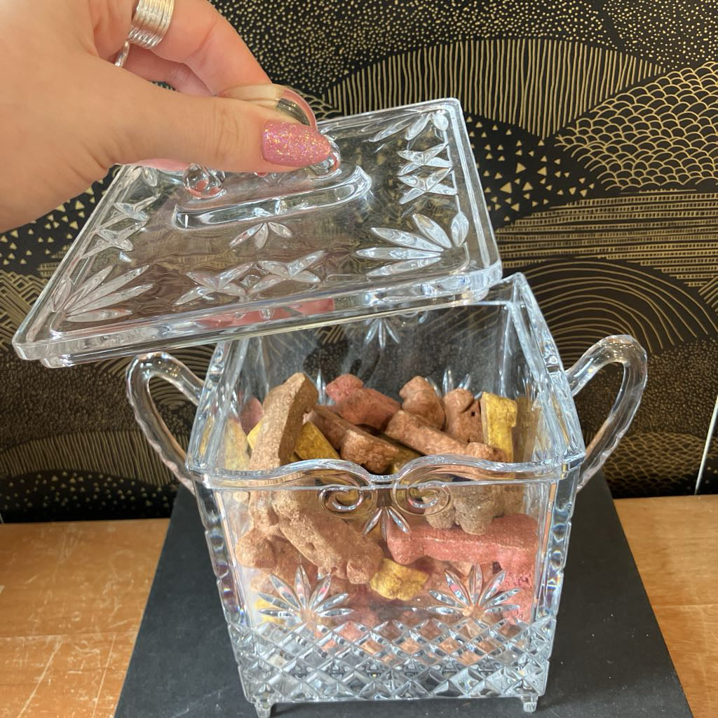 Decorative crystal container with lid filled with dog treats on a patterned surface.