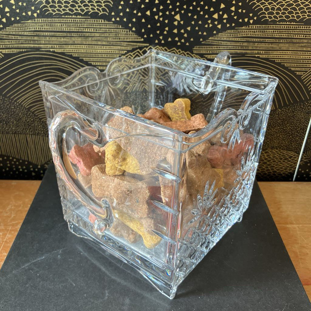 Clear glass container filled with dog treats on a black surface with a decorative gold background
