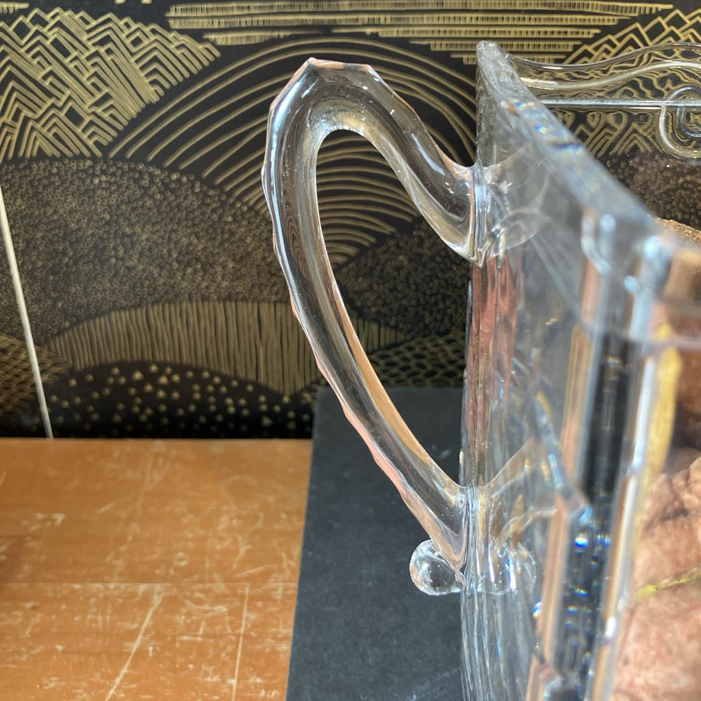 Clear glass pitcher with handle on a wooden surface
