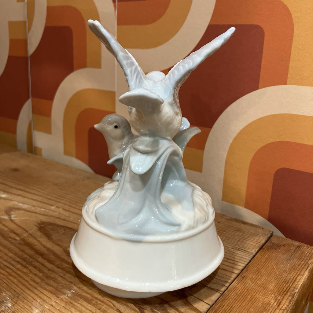 Decorative ceramic sculpture of birds on a wooden surface with a patterned wall in the background