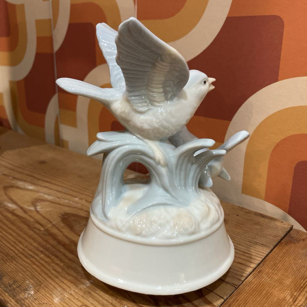White ceramic dove figurine on a wooden surface with a patterned wall in the background