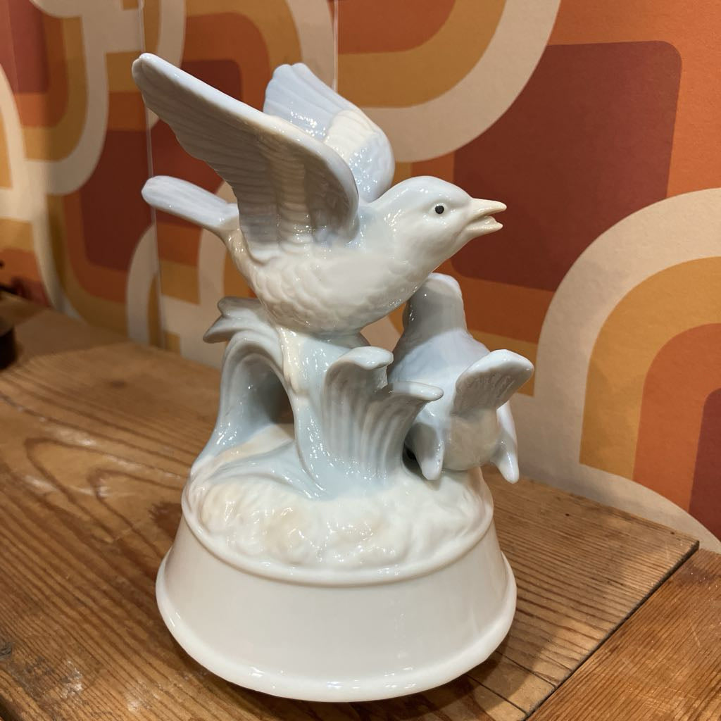 White ceramic bird sculpture on a wooden surface with a colorful abstract pattern in the background