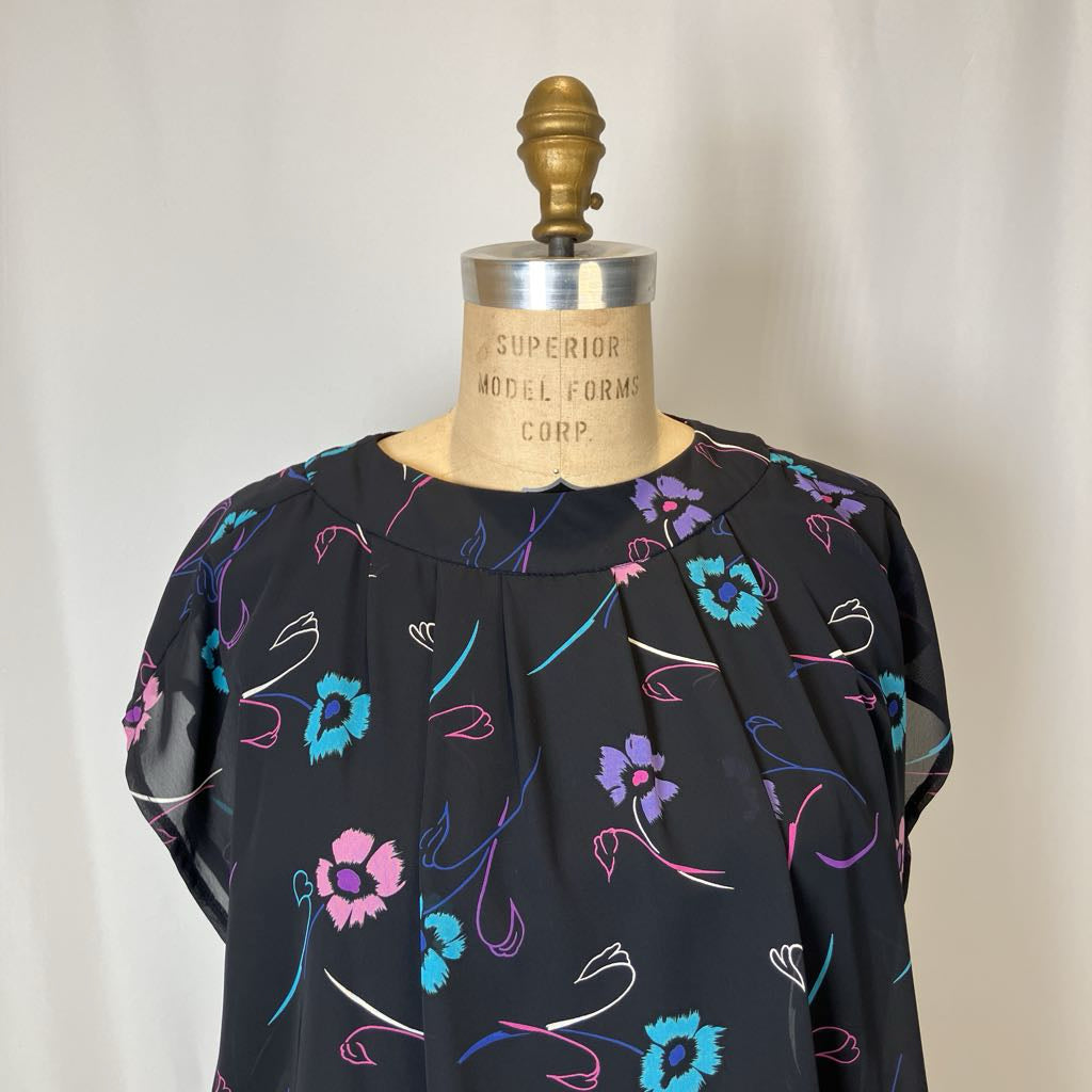 Black blouse with colorful floral patterns on a mannequin against a plain background