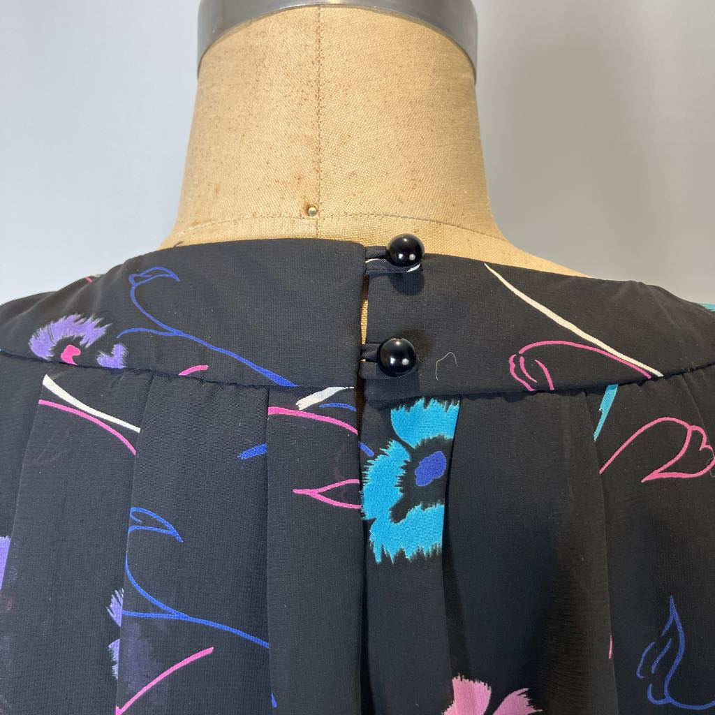 Black blouse with colorful abstract patterns on a mannequin against a gray background
