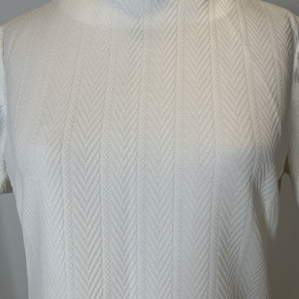 Close-up of a textured white sweater on a mannequin against a neutral background