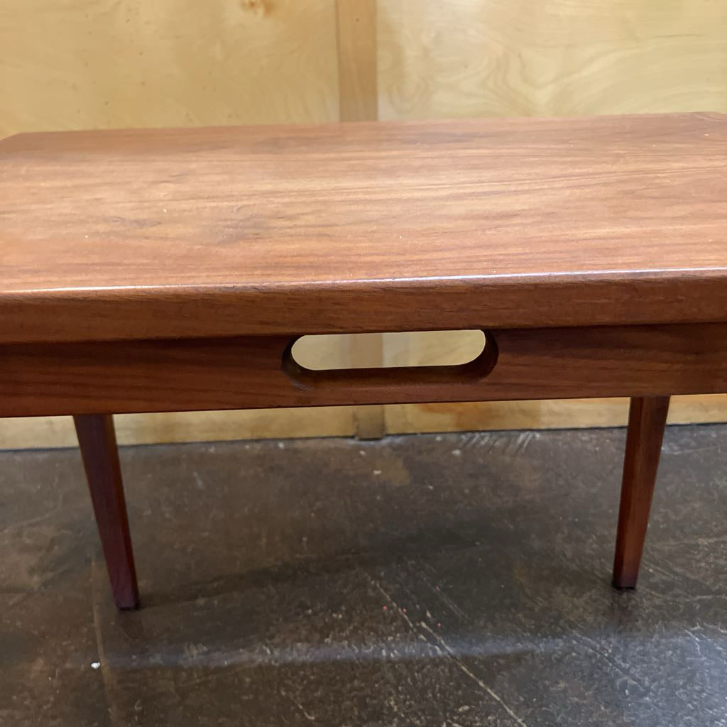 Wooden table with a handle on a tiled floor against a wooden wall.