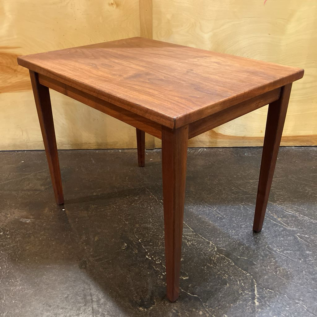 Wooden table with a brown finish on a dark floor against a beige wall.