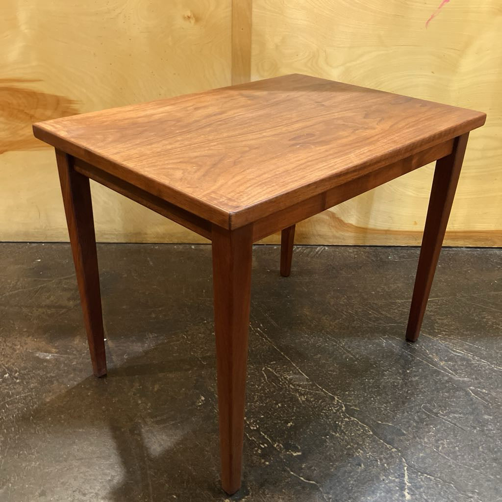 Wooden table with a rustic finish on a dark floor against a wooden wall.