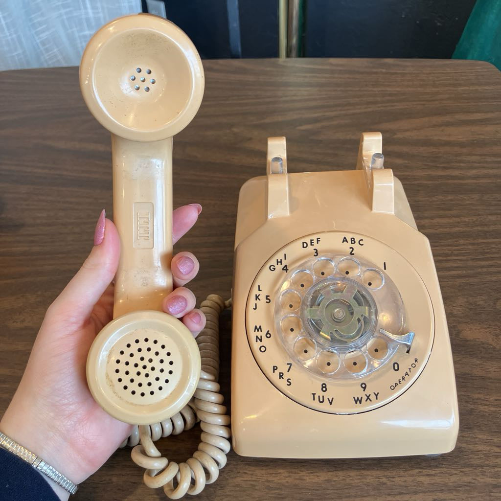 Beige rotary phone with handset on a wooden surface