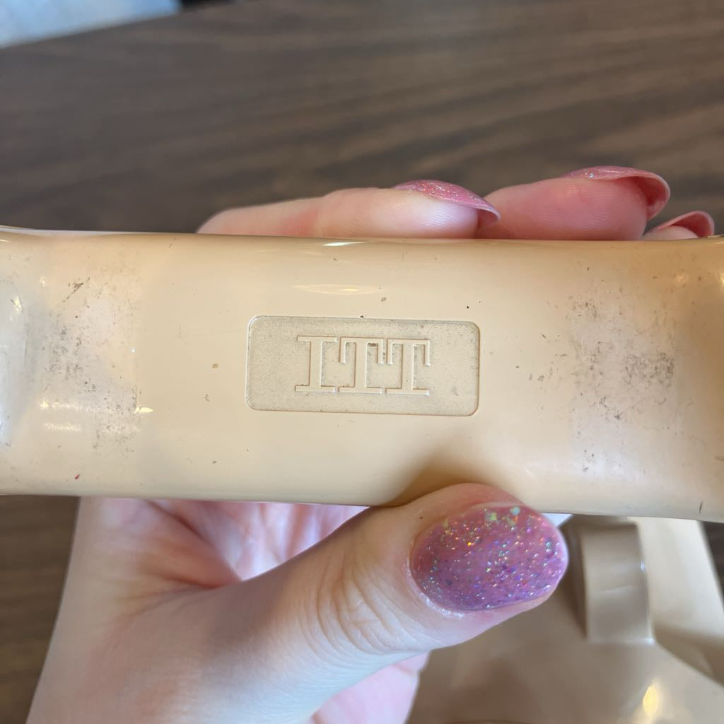 Hand holding a beige object with a visible brand logo on a wooden surface