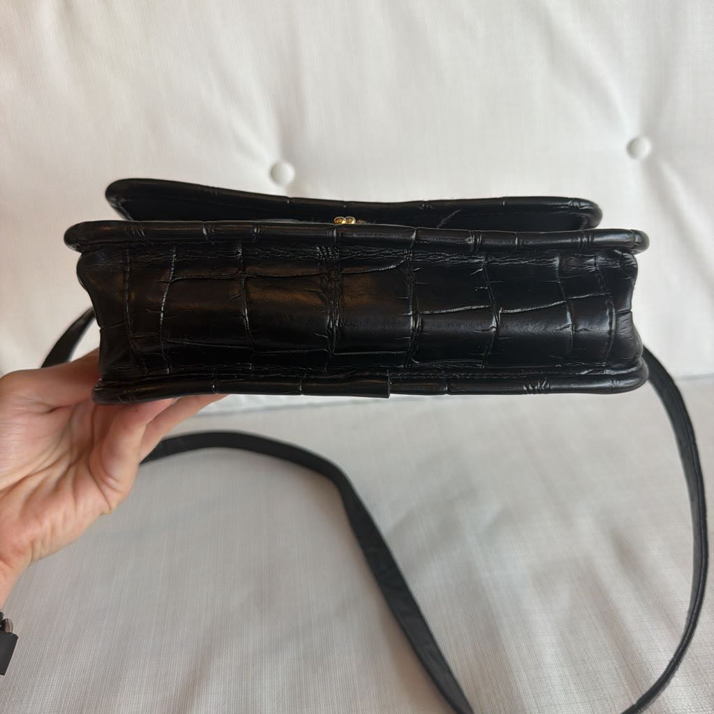 Black crocodile-patterned handbag held by a hand on a light gray background