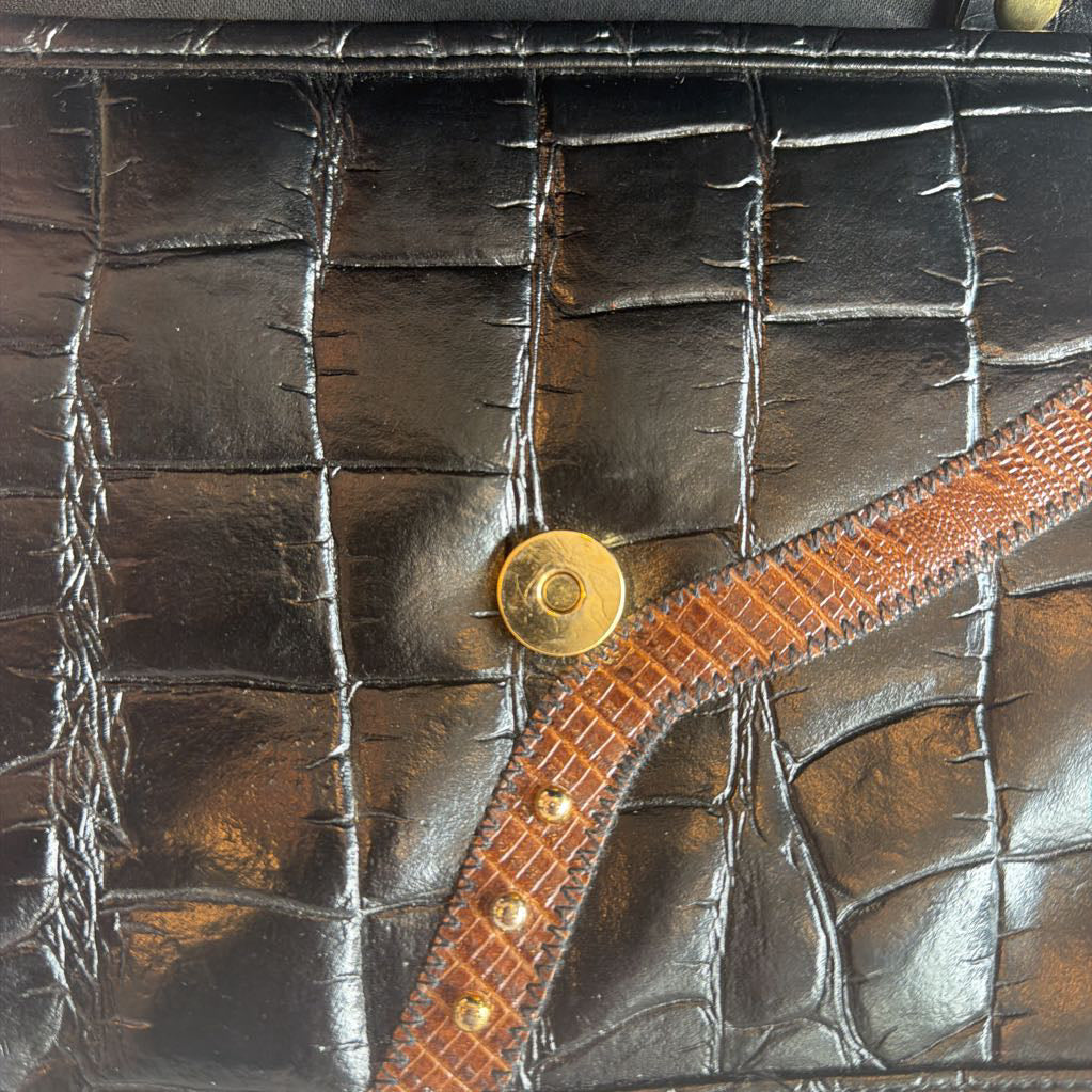 Close-up of a textured leather surface with a gold button and brown strap.