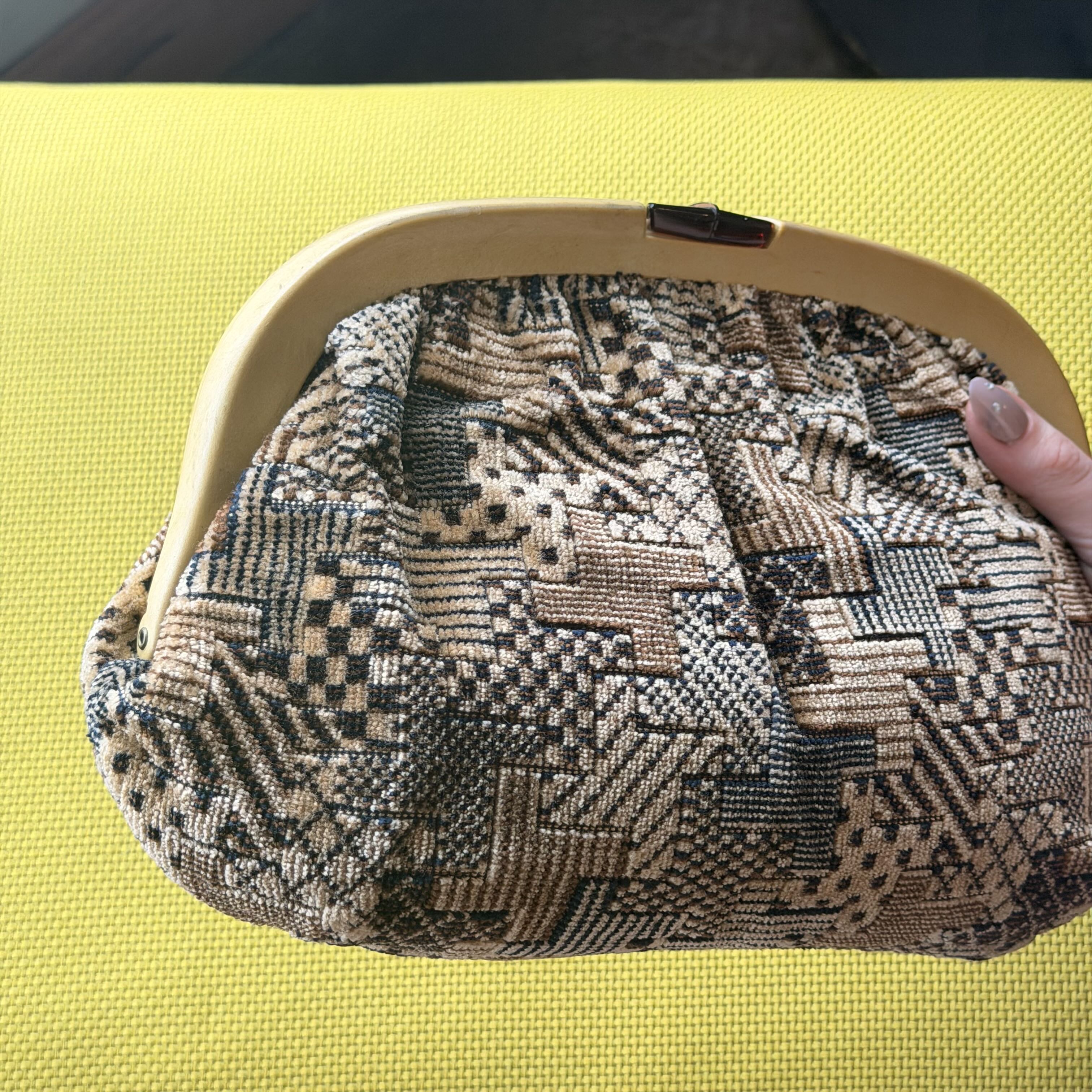 Patterned handbag held by a hand on a yellow surface