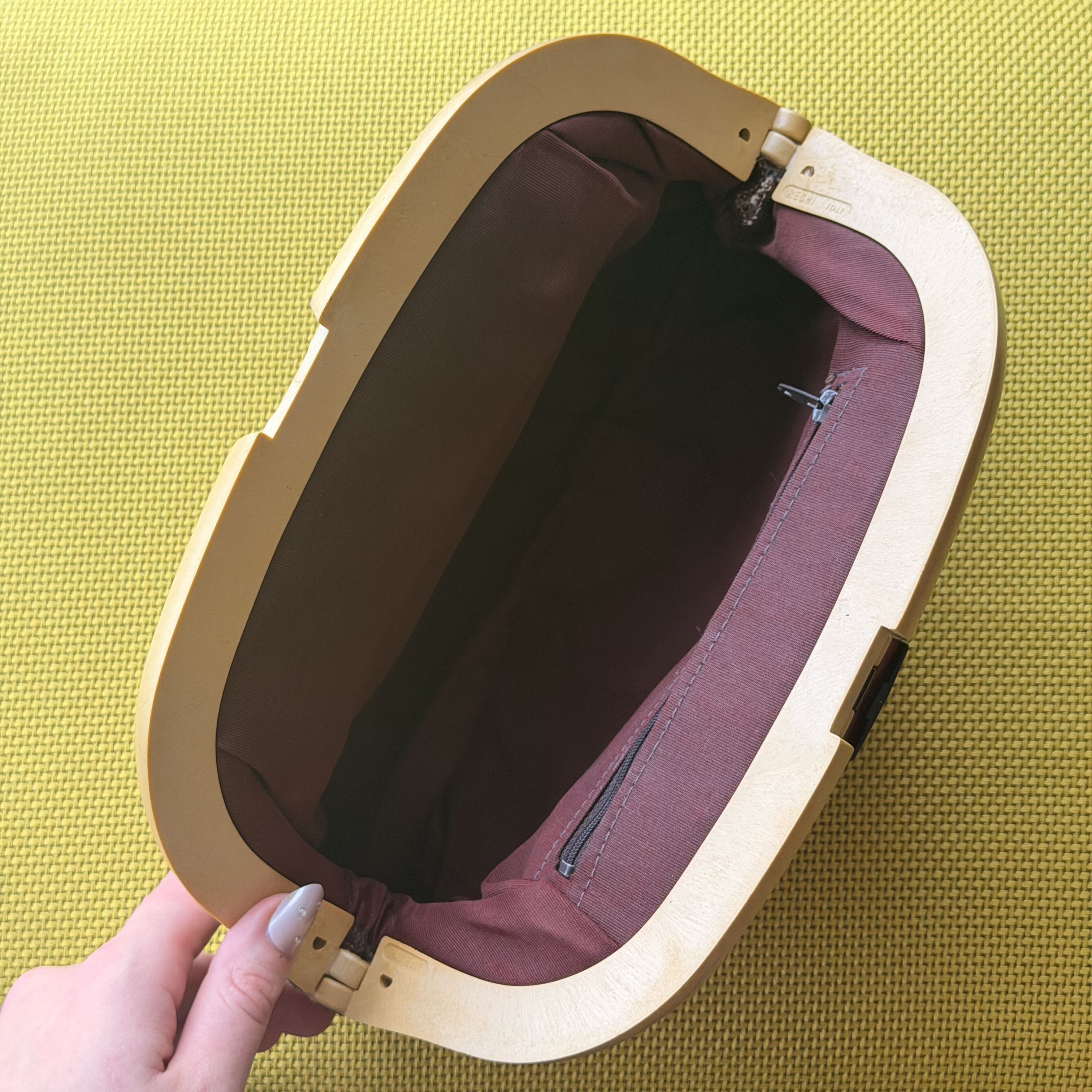 Open beige bag with maroon interior on a yellow background