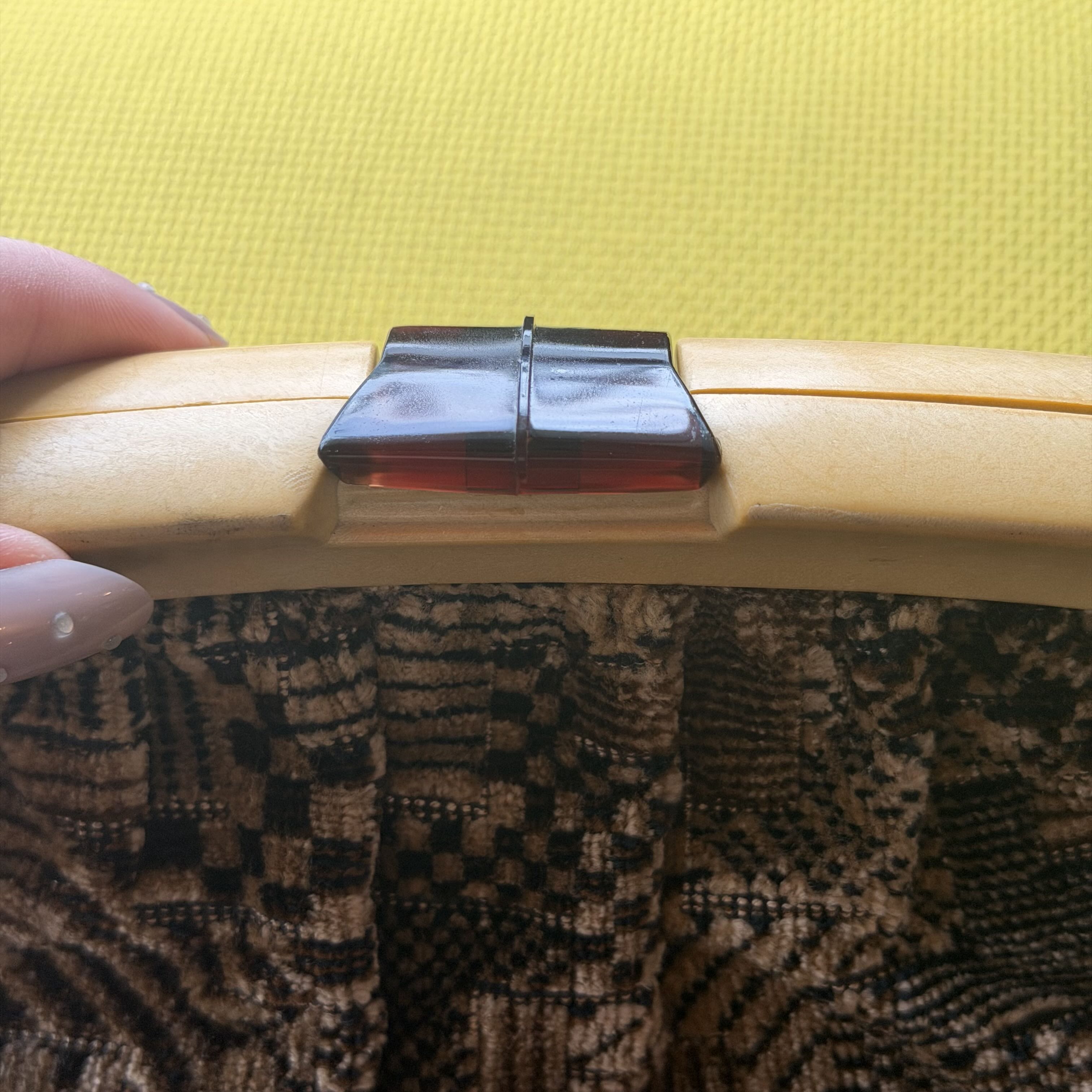 Hand holding a wooden object with a dark clip against a yellow and patterned fabric background