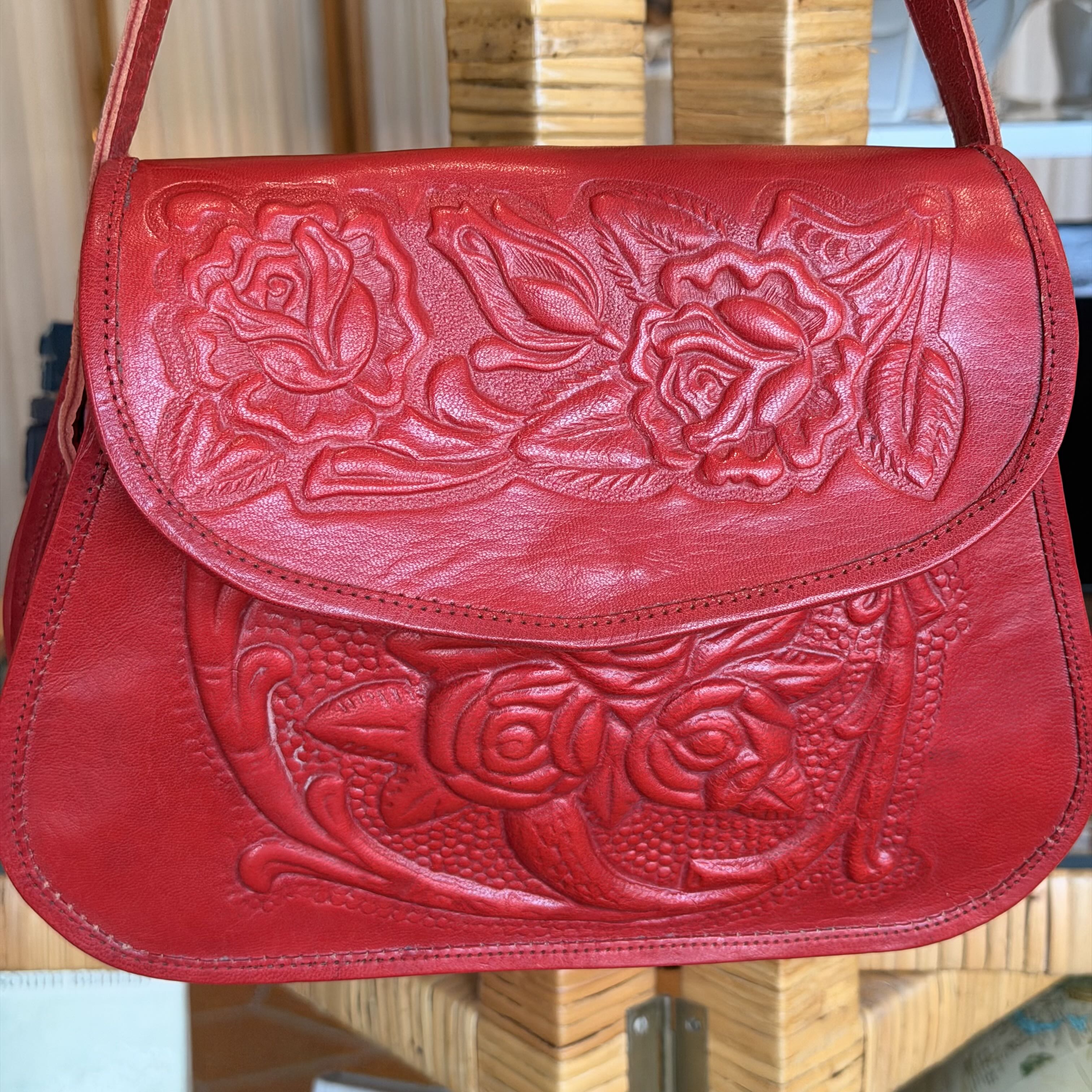 Red leather handbag with floral embossing on a wooden surface