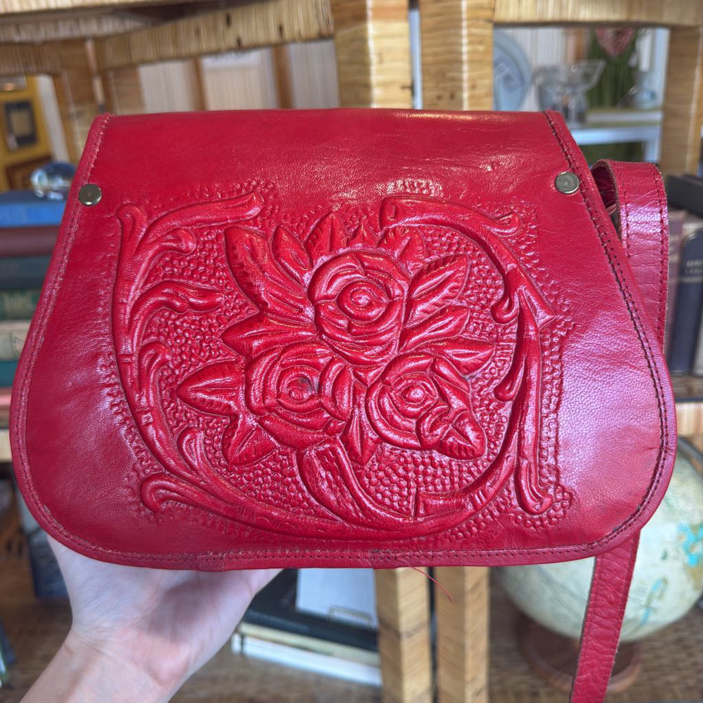 Red leather handbag with floral embossing held by a person.