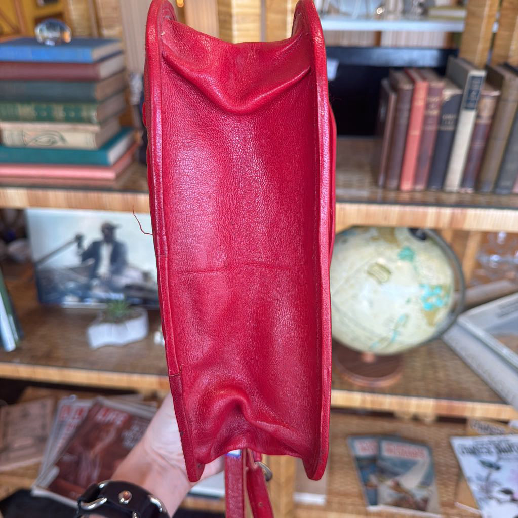 Red leather wallet held in front of a bookshelf with books and a globe.