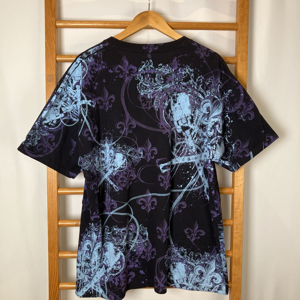 Black t-shirt with blue and white floral patterns on a wooden hanger against a beige wall.
