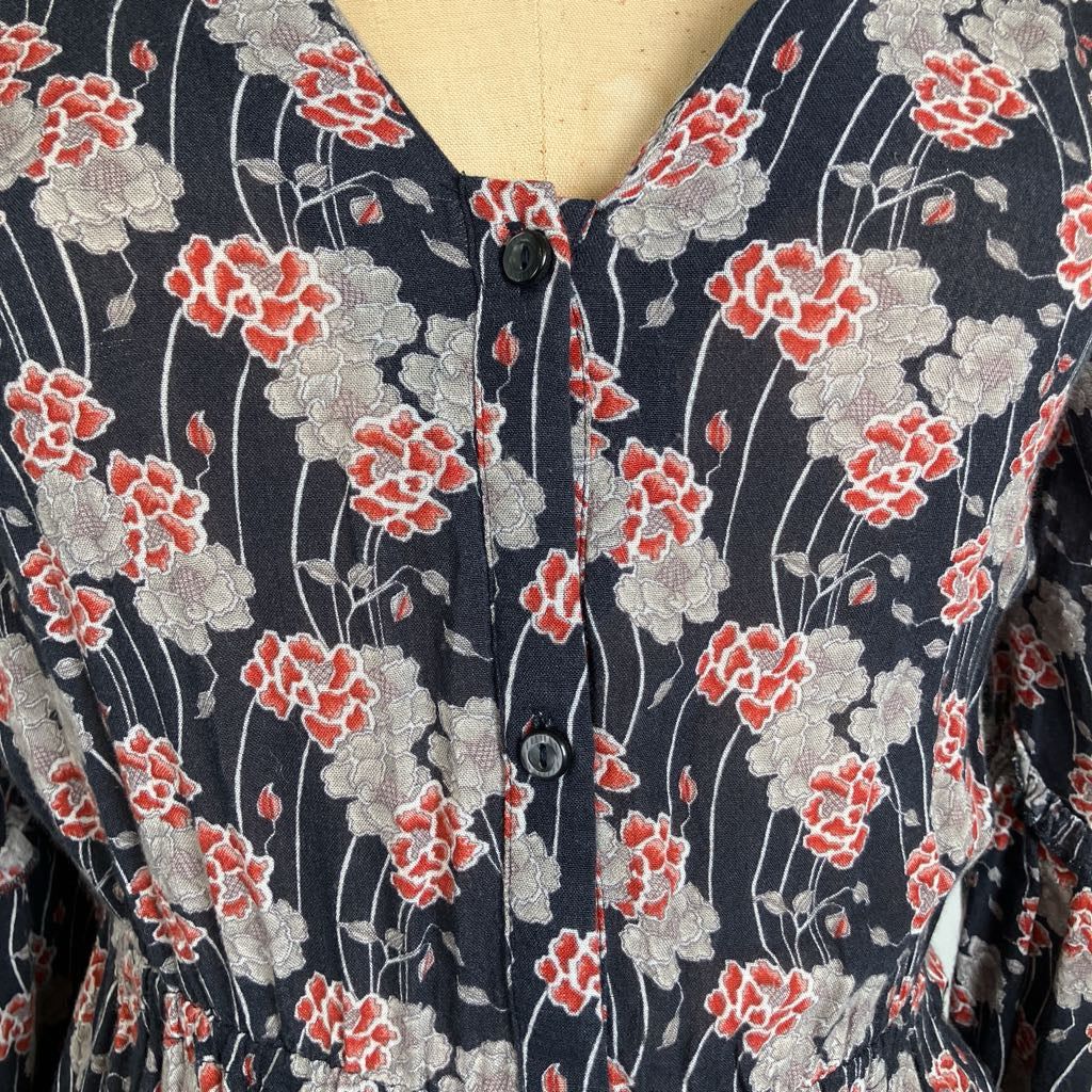 A close-up of a vintage floral dress on a mannequin, featuring a dark navy blue base with red and gray flowers, white stems, and a buttoned V-neckline.