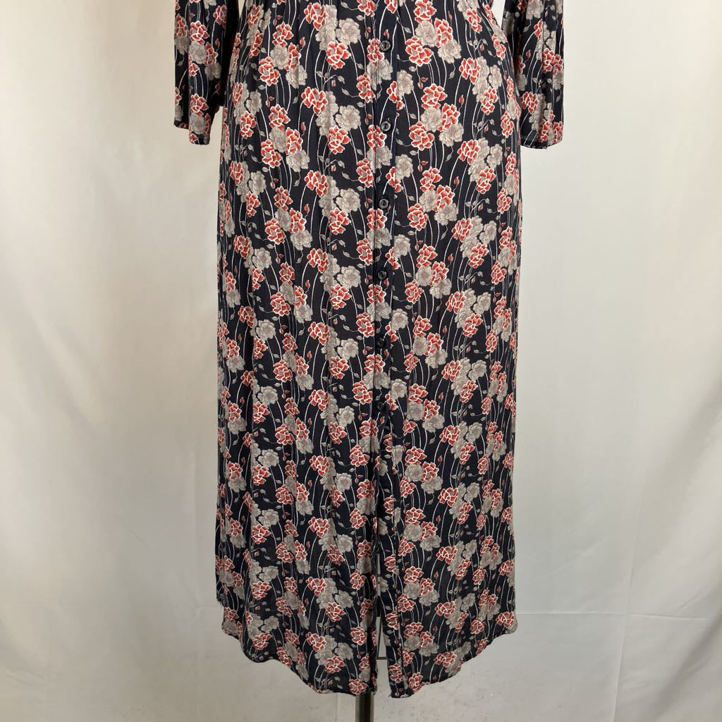 A long-sleeve midi dress with a dense floral print, displayed on a mannequin against a white fabric backdrop.