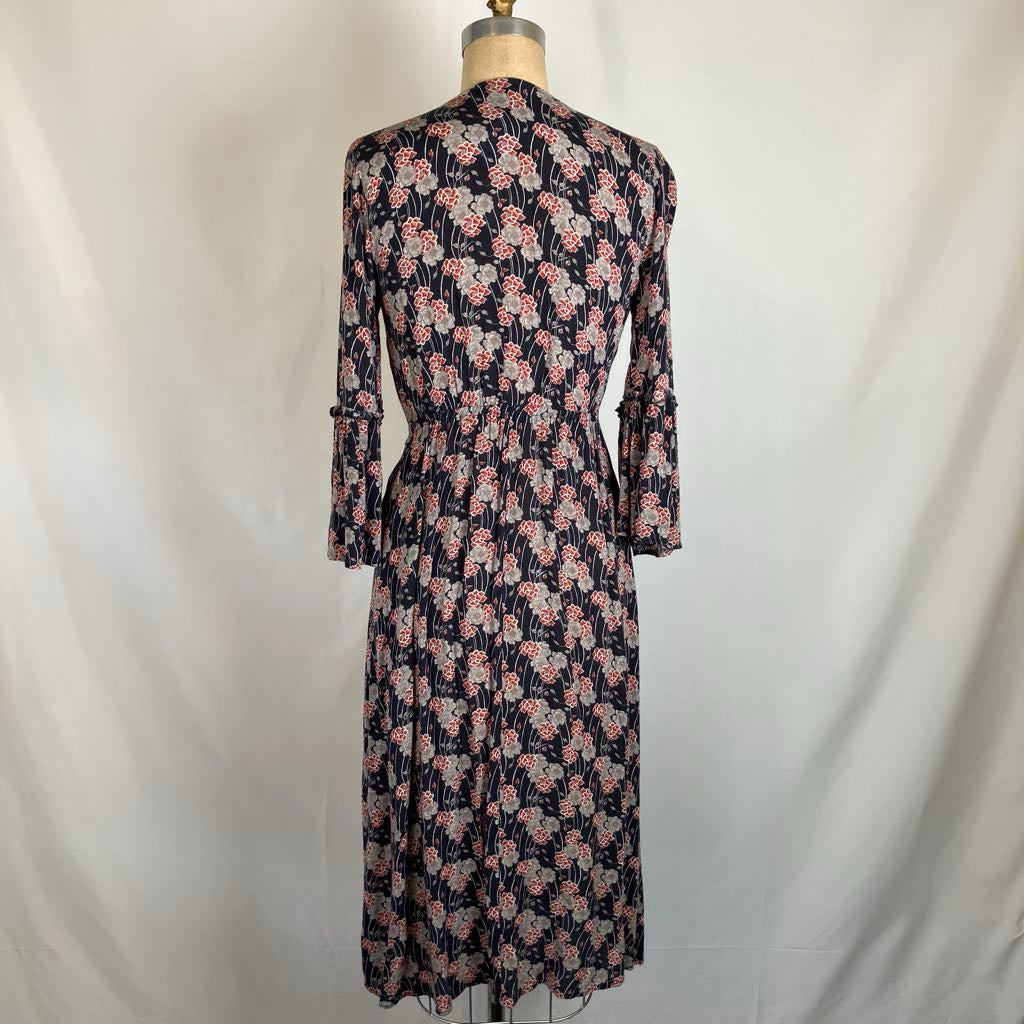 A long-sleeve midi dress with a pink and white floral pattern on a dark navy background, displayed on a dress form against a white fabric backdrop.