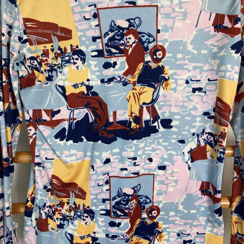 A close-up of a patterned garment or fabric featuring vintage-style illustrated figures in a cafe or lounge scene, with yellow, navy, brown, and pale pink tones on a light background.