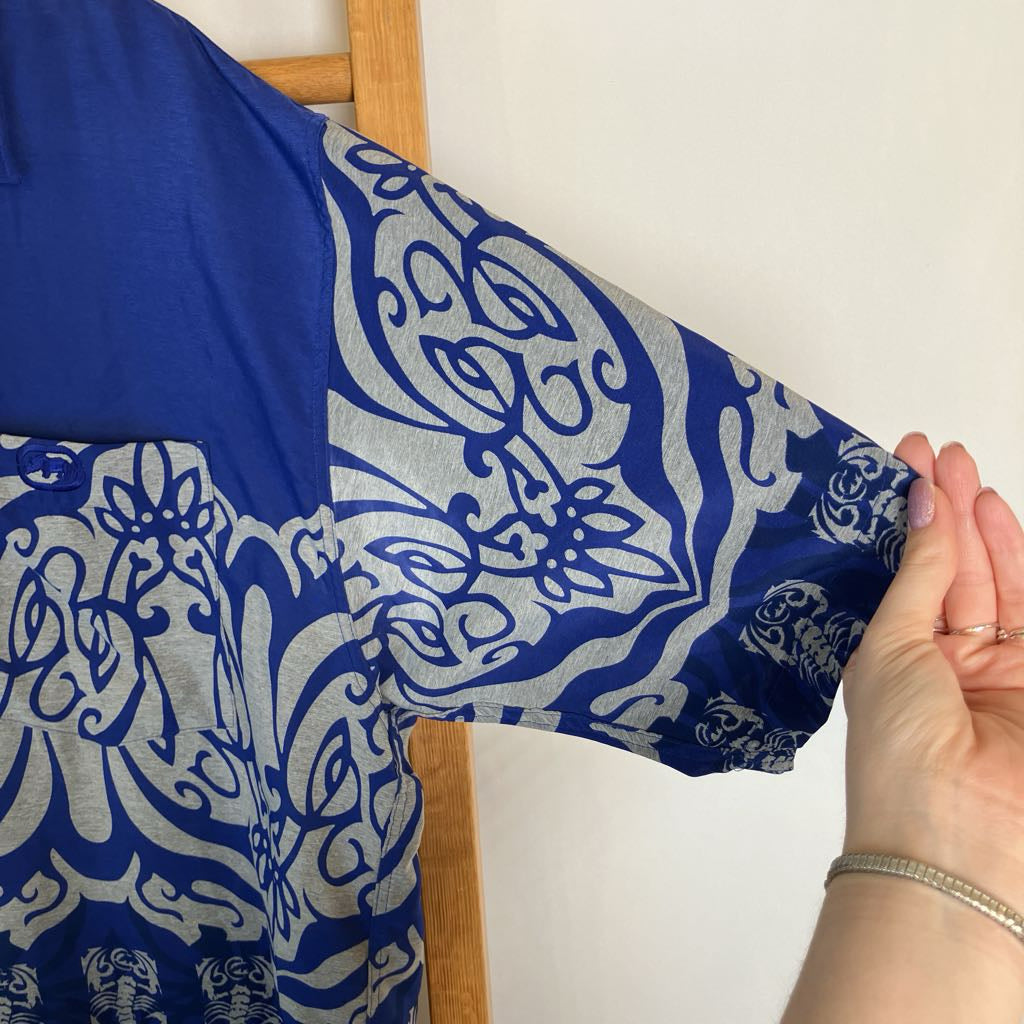A close-up of a blue and gray patterned garment being held by a hand, showing a detailed view of the fabric pattern and sleeve.