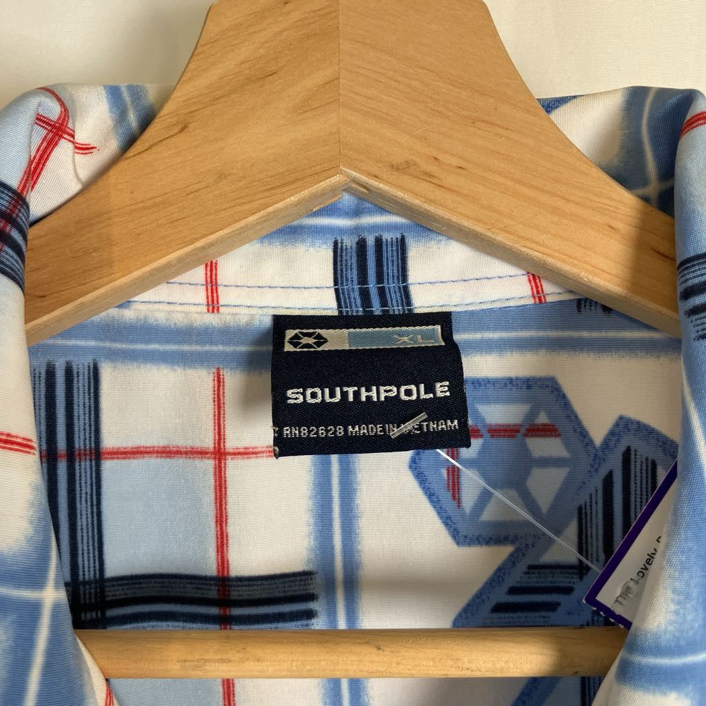 A close-up of a Southpole fleece blanket with a blue, white, and red geometric plaid pattern, draped over a wooden hanger.