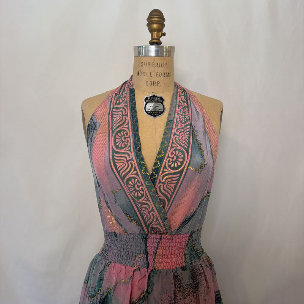 A vintage halter dress displayed on a wooden mannequin torso. The dress features a vibrant, multicolored patchwork print with pink, teal, green, and orange tones, decorated with geometric and floral patterns.