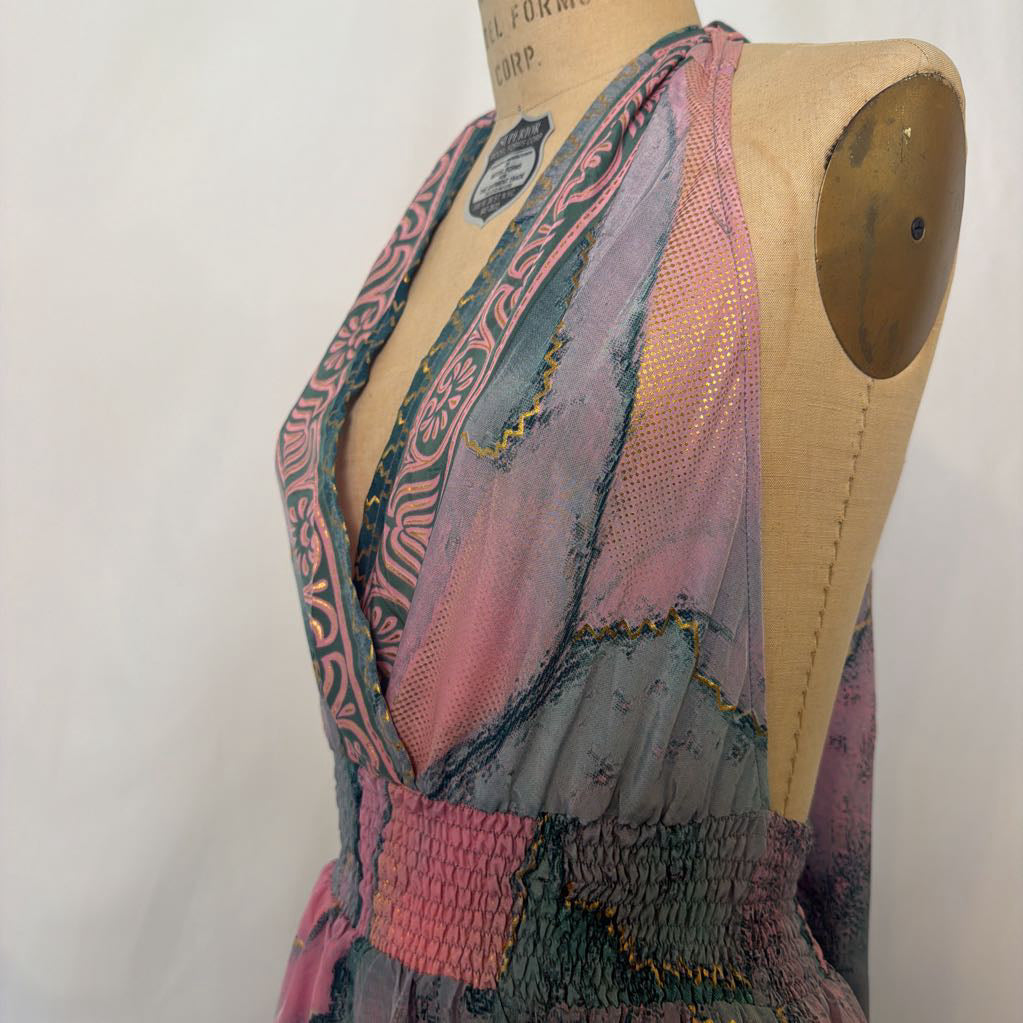 A multicolor patchwork mesh and tulle dress displayed on a wooden dress form mannequin. The dress features a smocked waist and a deep V-neckline with patterned pink, teal, and gray panels.