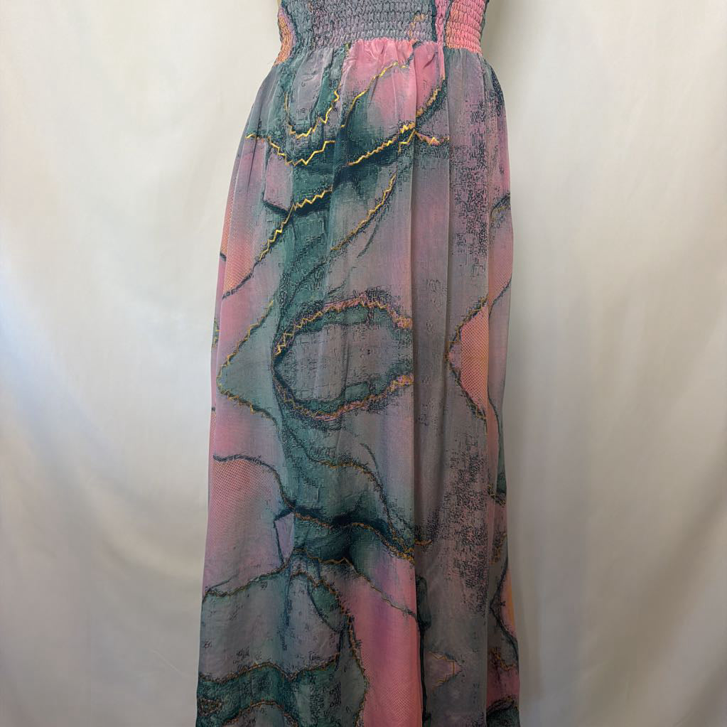 A sleeveless maxi dress with a smocked bodice and a flowing, semi-sheer skirt featuring an abstract marbled pattern in pink, teal, and gray with gold sequin accents, shown against a plain off-white background.