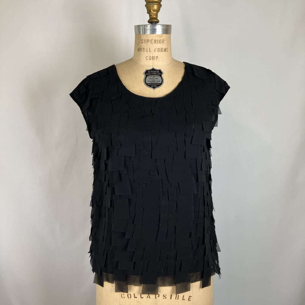 A black sleeveless fringed top displayed on a beige dress form mannequin against a light gray fabric backdrop.