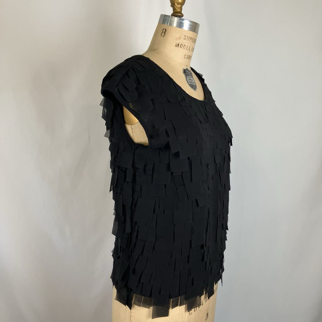 A black sleeveless fringe top displayed on a vintage dress form mannequin against a light gray background.