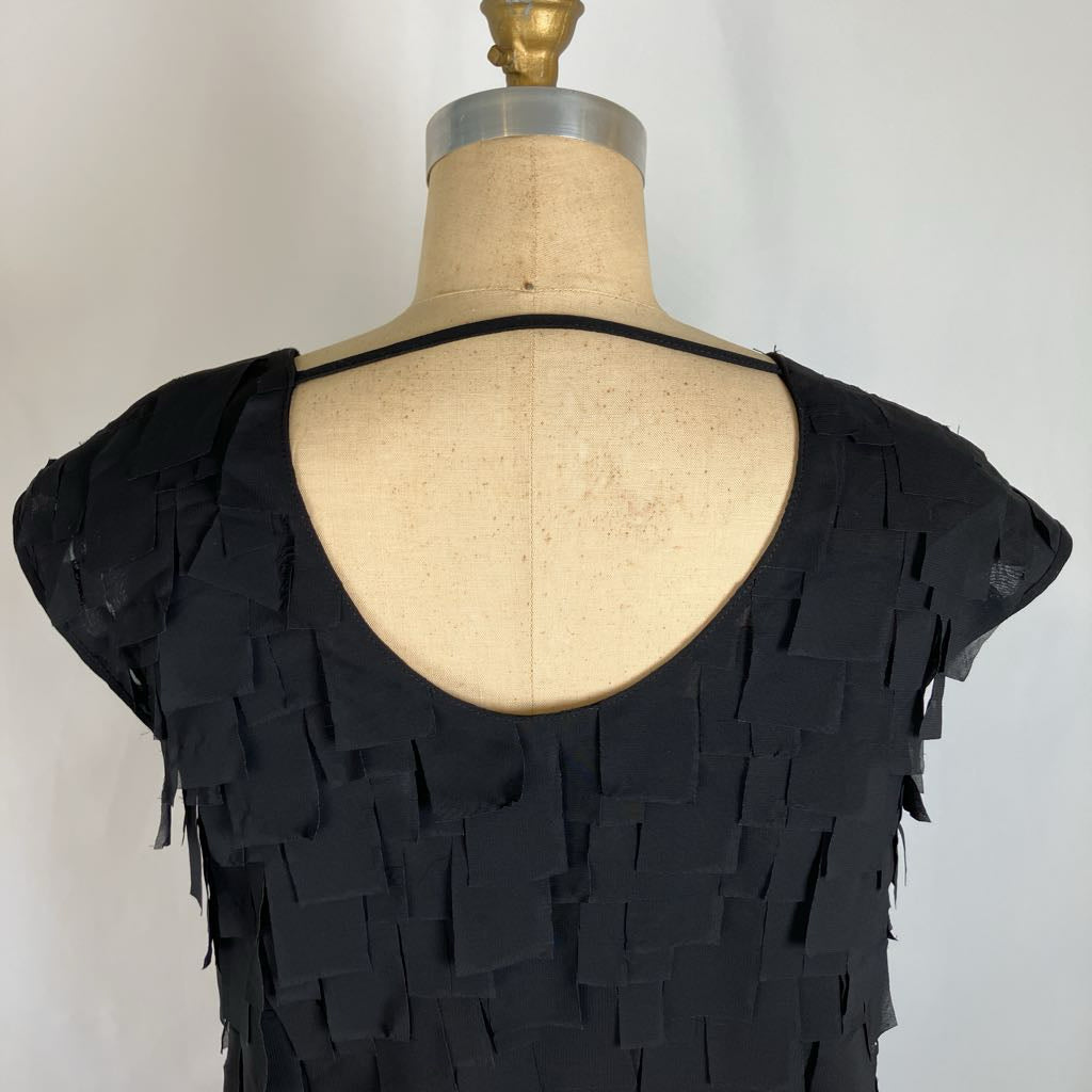 Black fringed top displayed on a dress form mannequin, showing the back view with a deep scoop neckline and layered rectangular fringe details.